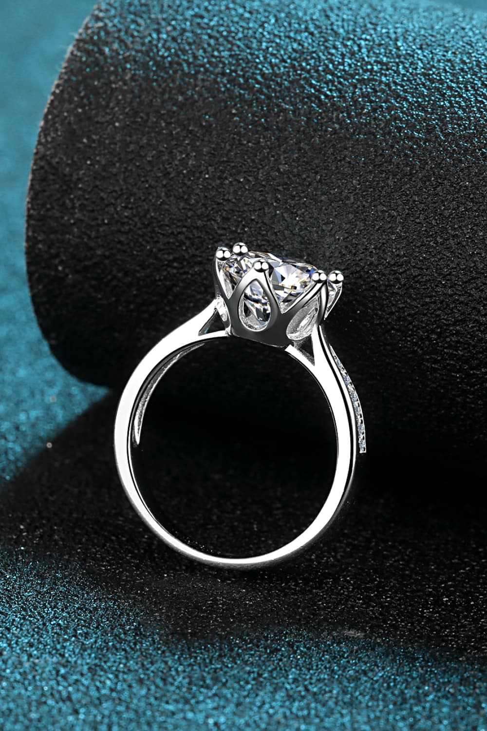 3 Carat Moissanite Rhodium-Plated Side Stone Ring displaying a modern minimalist design on a textured teal surface.