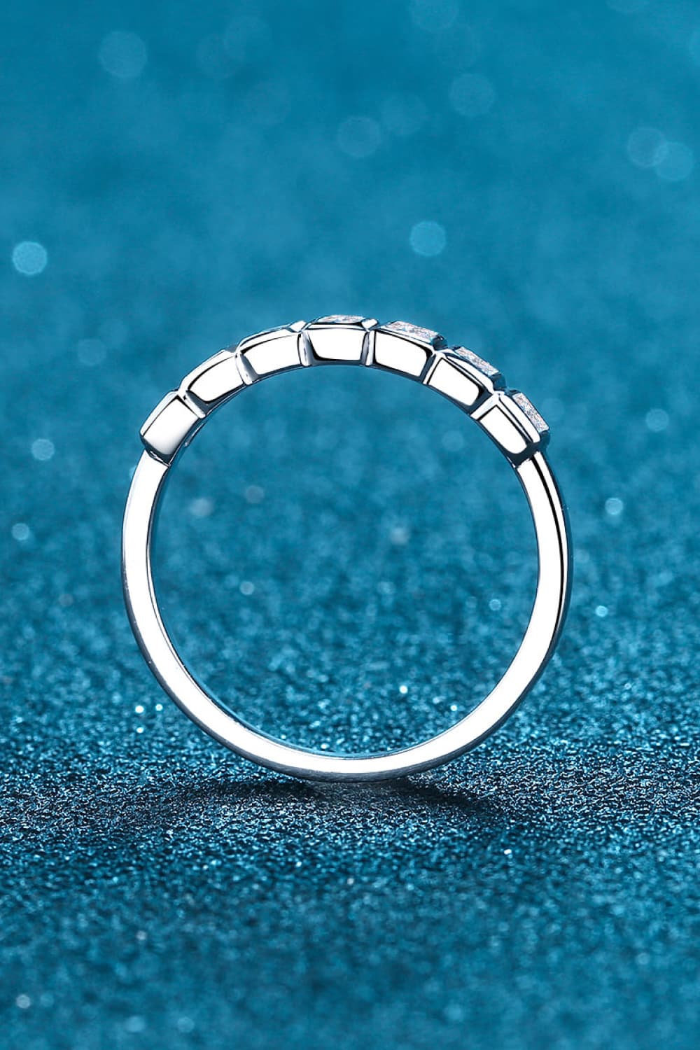 Moissanite Rhodium-Plated Half-Eternity Ring displayed on blue sparkling surface.