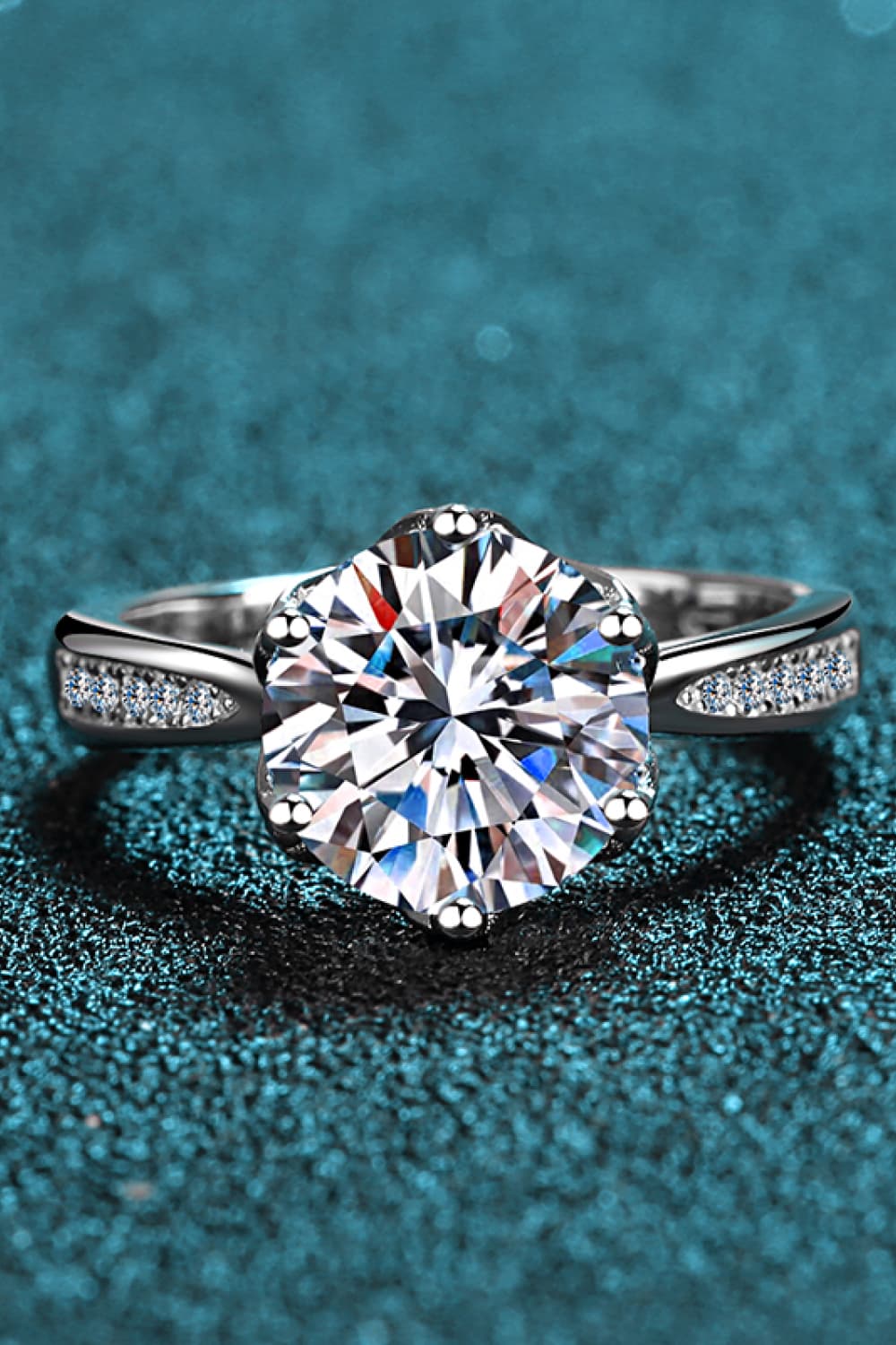 3 Carat Moissanite Rhodium-Plated Side Stone Ring with sparkling center stone and side accents on a teal background.
