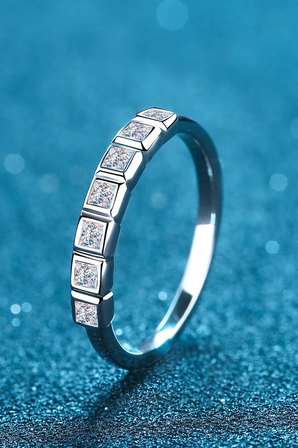 Moissanite Rhodium-Plated Half-Eternity Ring with sparkling gems on a blue glitter background.